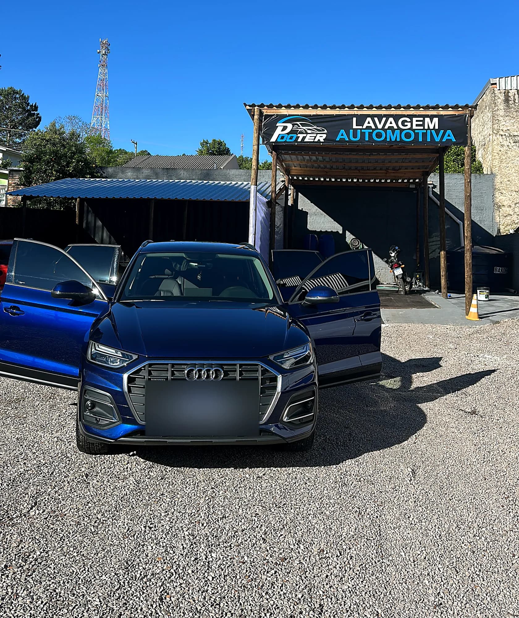 Fachada do lava-rápido Pooter Lavagem Automotiva, com a placa da empresa e um SUV azul no pátio